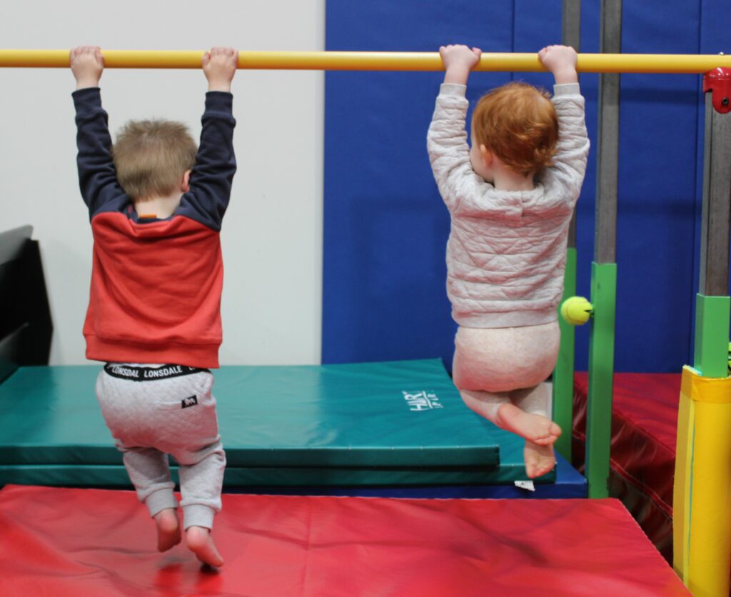 Two small children holding onto a yellow bar with their legs dangling